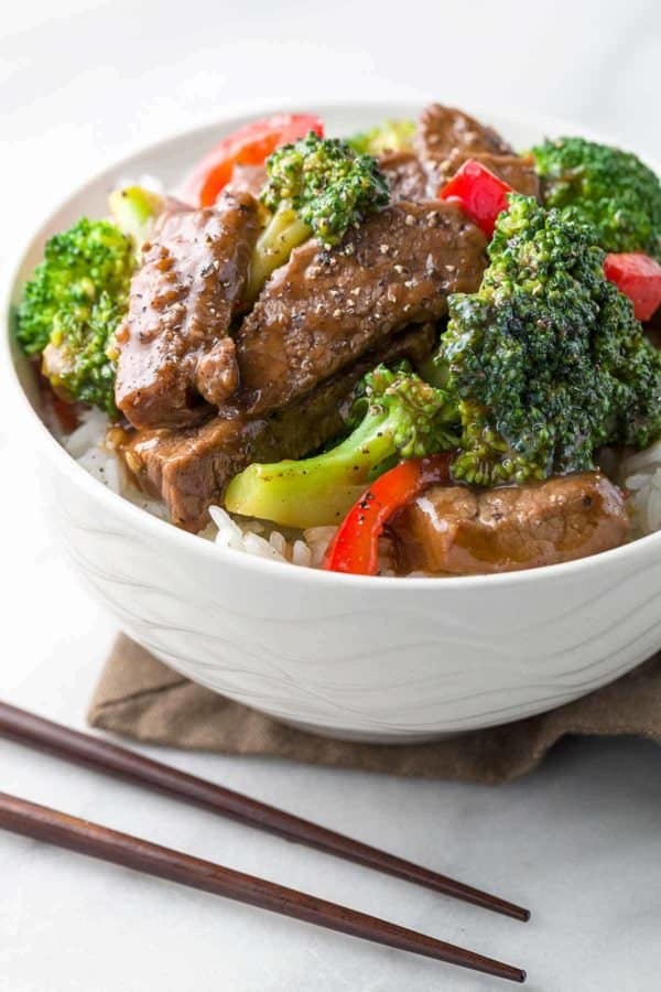 白碗西兰花牛肉用筷子在桌上炒