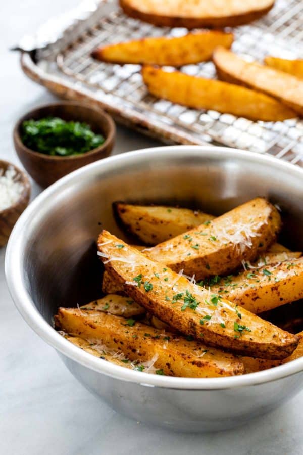 新鲜切碎的欧芹和磨碎的帕尔马干酪混合在一个碗用被烘烤的土豆楔子