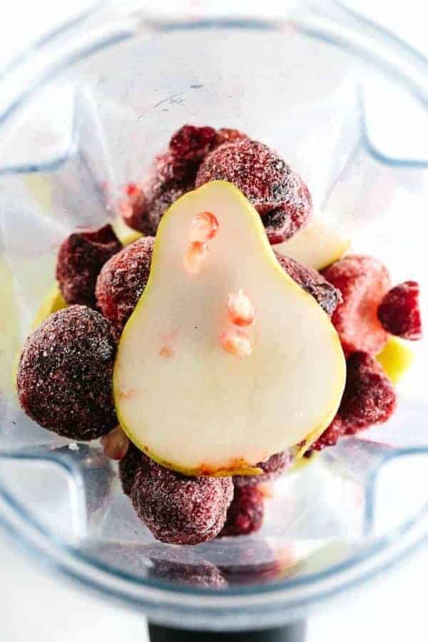 搅拌机容器装满冰冻的石榴和切片的梨