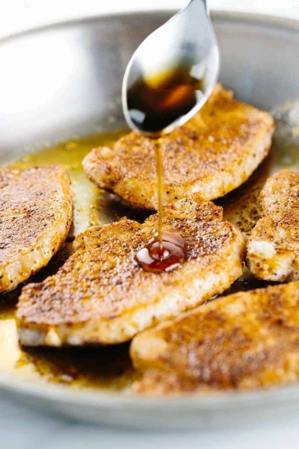 用勺子将枫糖浆倒在正在平底锅中烹煮的猪排上