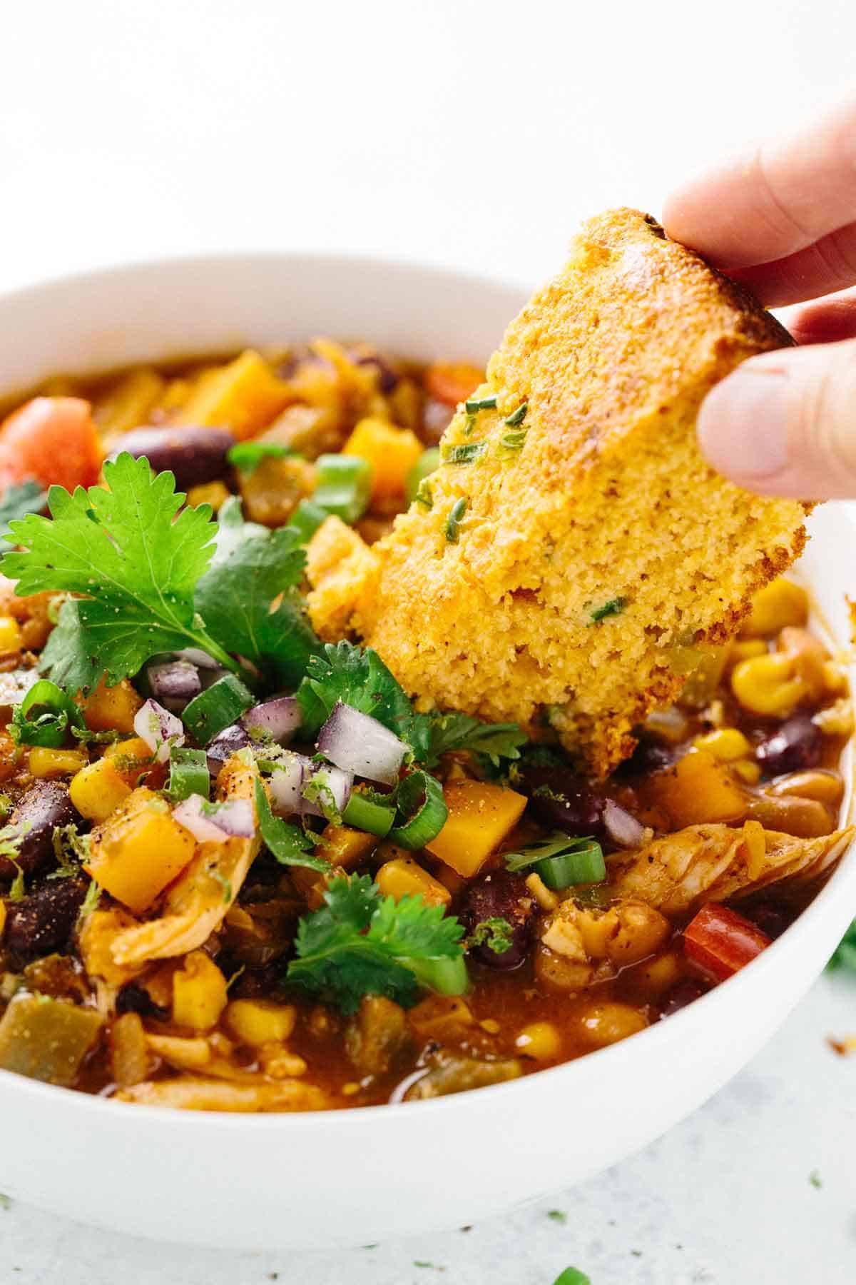 手指拿着玉米面包,把它泡在一碗鸡肉辣椒里