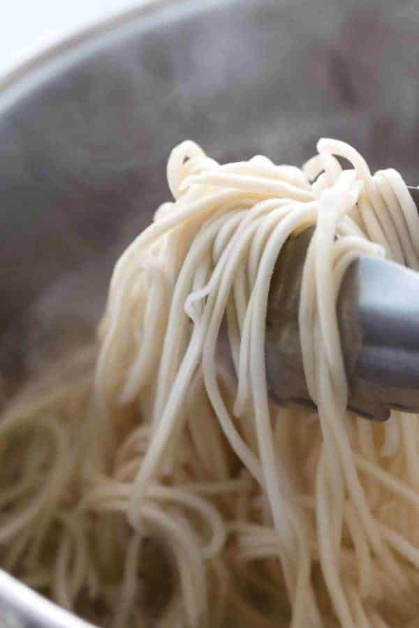 举煮熟的鸡蛋面条的金属钳子从沸腾的罐水中