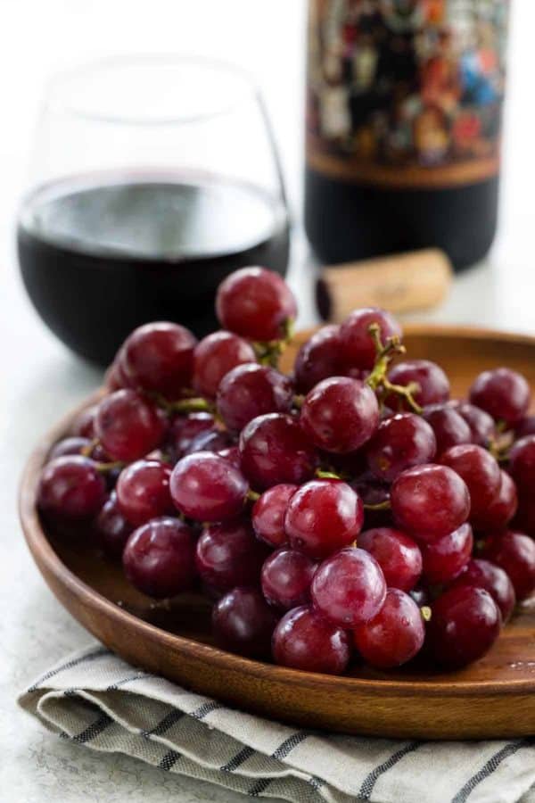 在一块木板材的红葡萄有一杯红葡萄酒在背景中