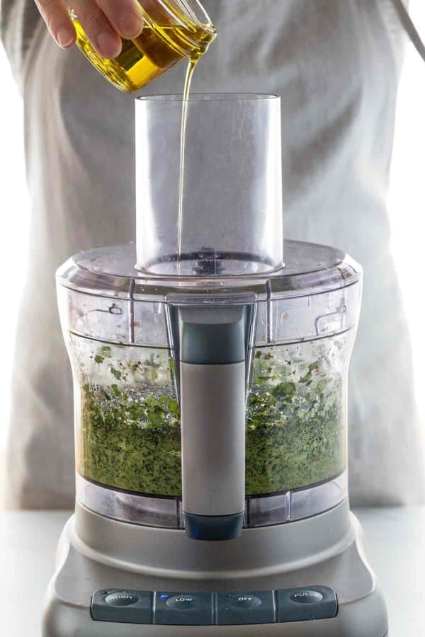 将一杯油倒入食品加工机的饲料管中的人