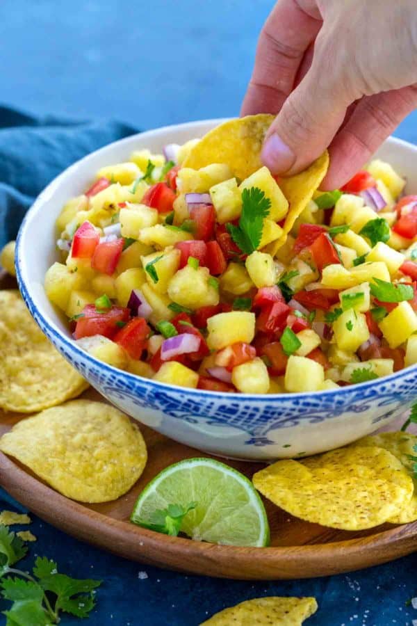 浸洗玉米粉薄烙饼芯片的手的照片到一碗菠萝辣调味汁