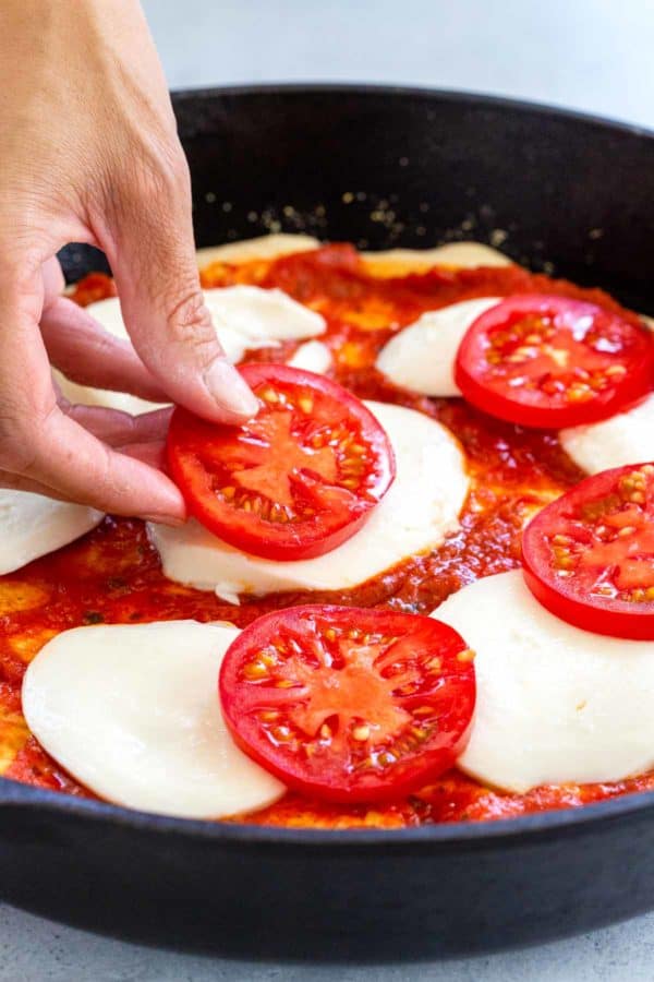 将蕃茄切片放在马苏里拉片顶部的人