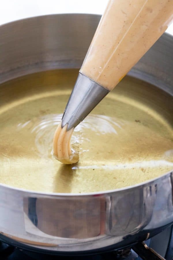 一个带星形尖头的酥皮袋把面团倒进一锅油里