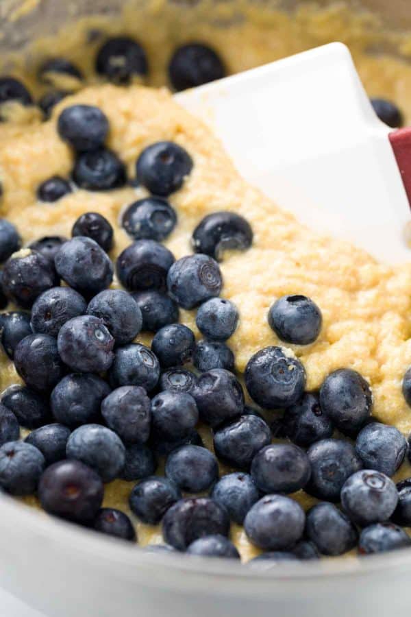 Several blueberries being mixed into a cornbread batter using a white spatula