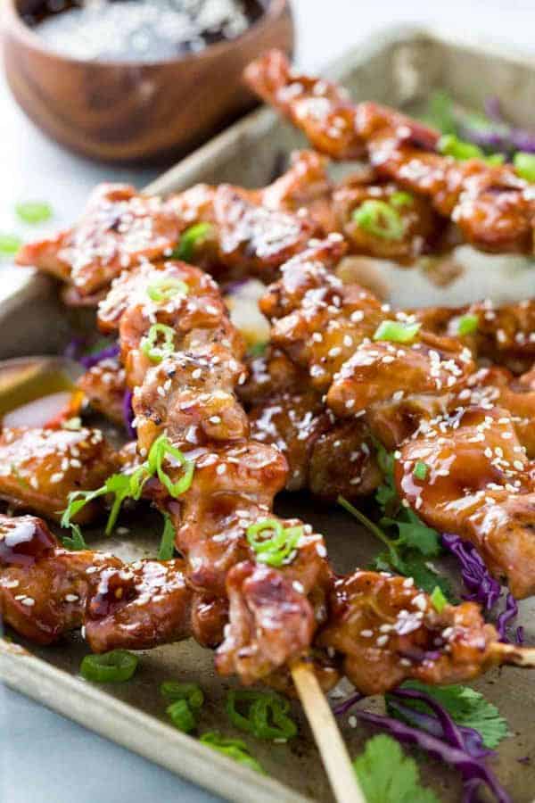 一块带有几个烤鸡串的纸锅，玉米酱酱和芝麻