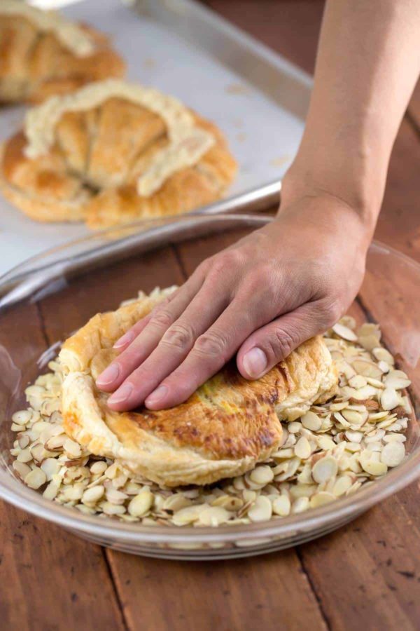 hand pressing down on a croissant in a bowl of almonds