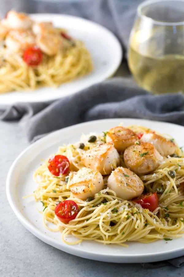 一盘烤扇贝和意大利面配上一杯白葡萄酒