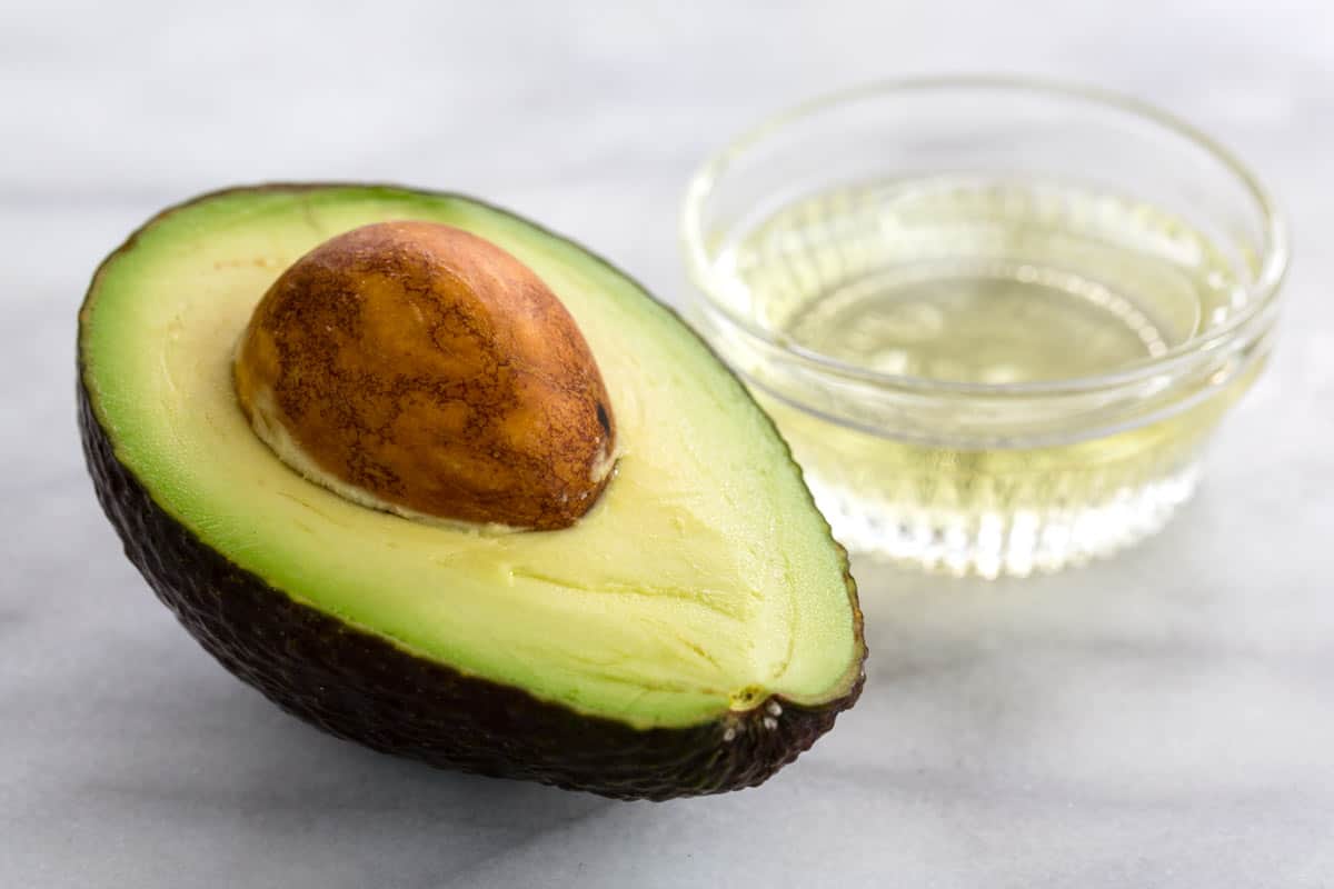 Cut open avocado and avocado oil in glass.