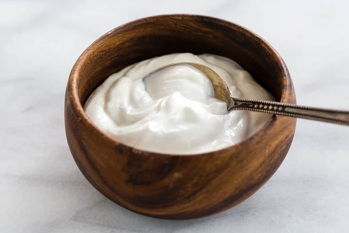 Greek yogurt in a wooden bowl with a spoon on top.