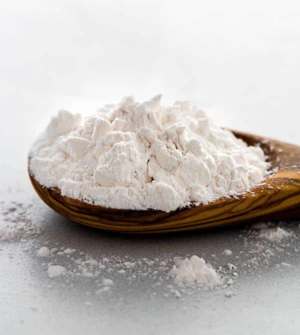 Closeup photo showing clumps of white arrowroot powder on a wooden spoon