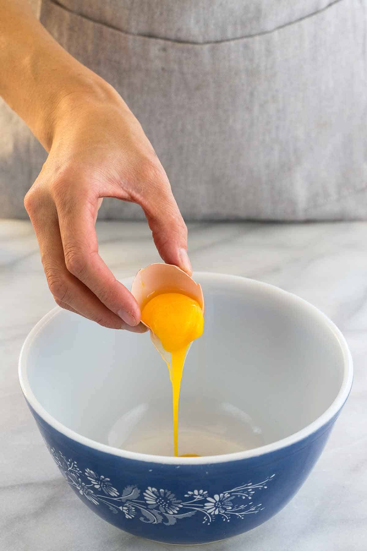 从一个破裂的鸡蛋加入蛋黄的手进入碗