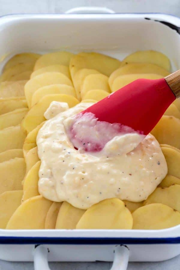 将一层奶油调味汁传播在砂锅盘的薄薄切片土豆的铲子