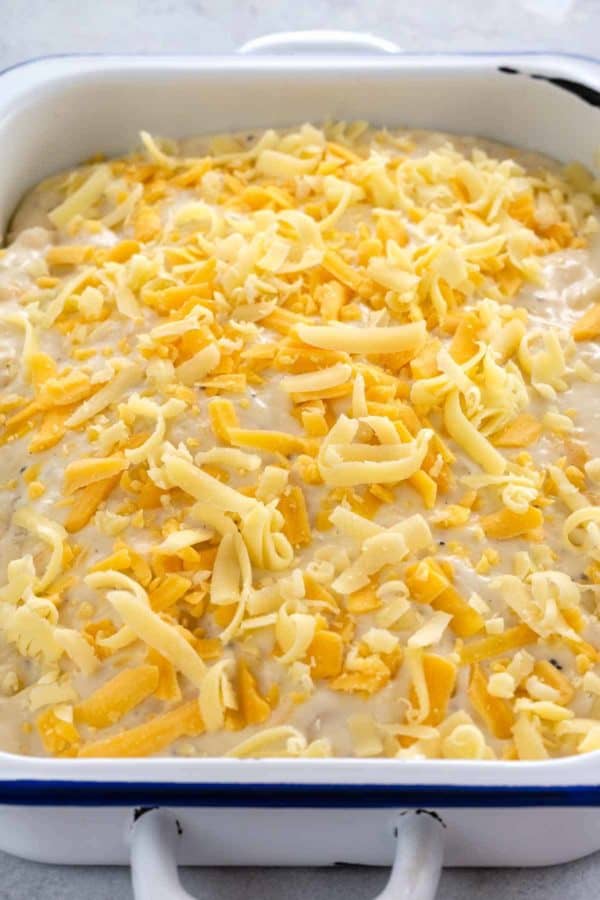 磨碎的gruyere和锋利的切达干酪洒在未煮过的土豆au gratin casserole顶上