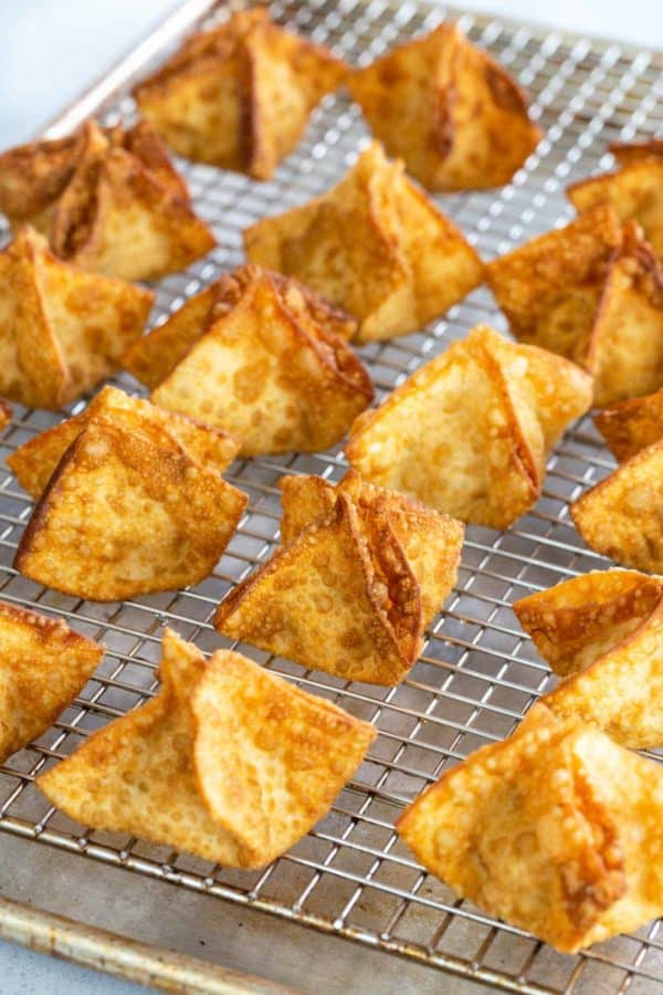 Several crab rangoon cooling on a wire rack after deep frying.