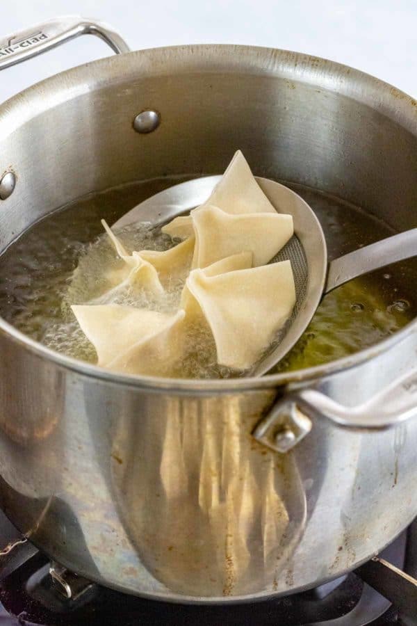 Steel spider strainer lowering four crab rangoons into a stockpot of hot oil.