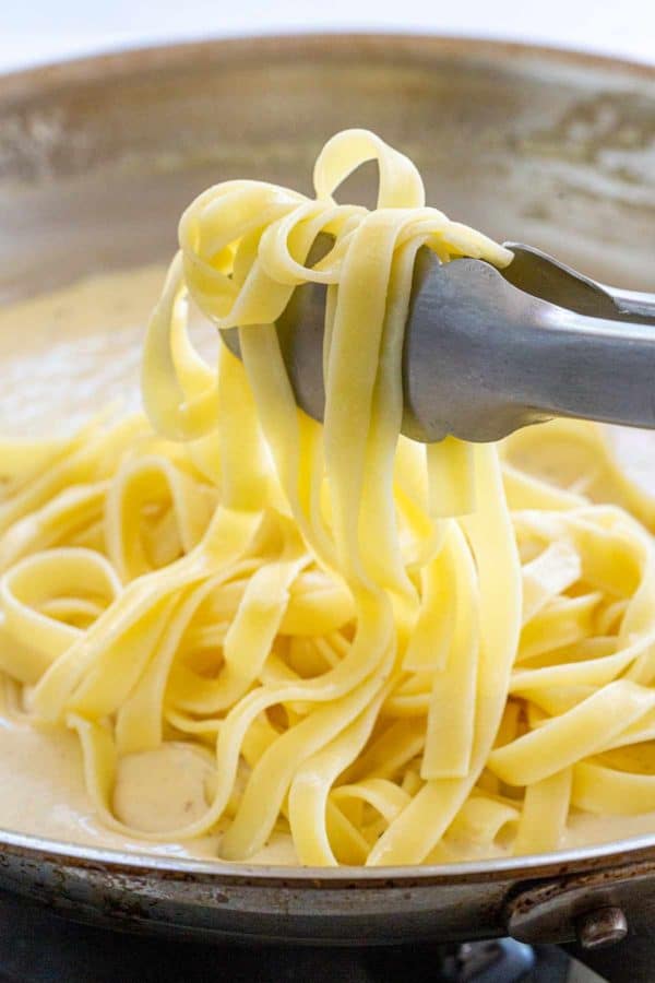 fettuccine noodles being put into a pan with alfredo sauce