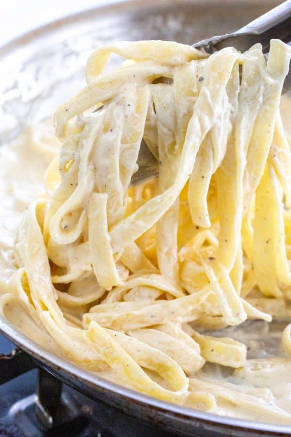 tongs mixing fettuccine with a creamy white sauce