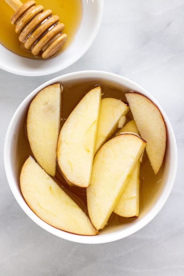 Sliced apples in a bowl of honey and water solution.