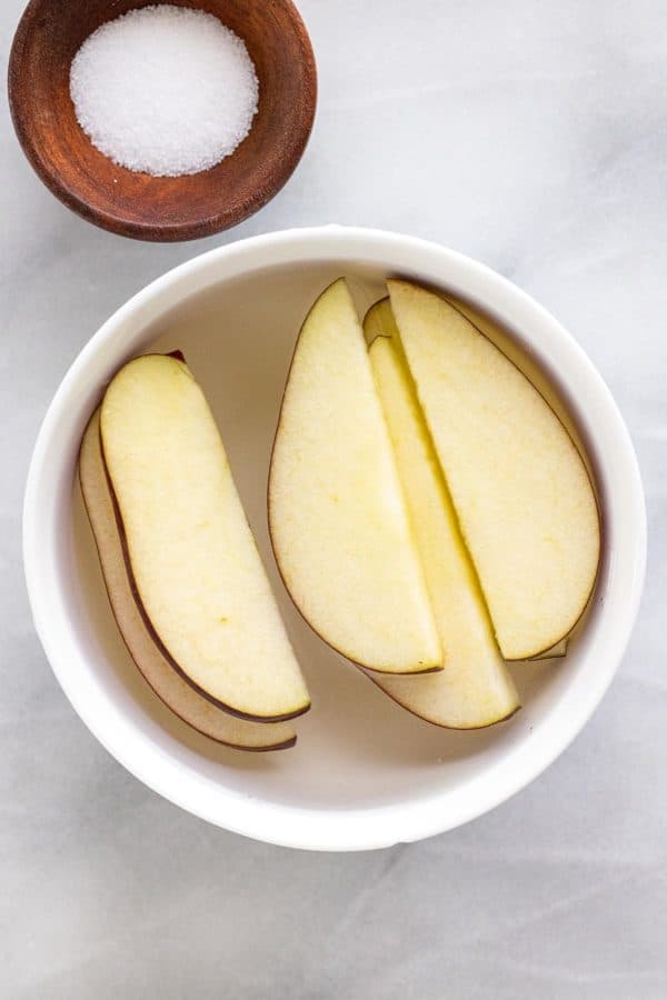 Sliced apples being treated in a bowl of salt water solution.