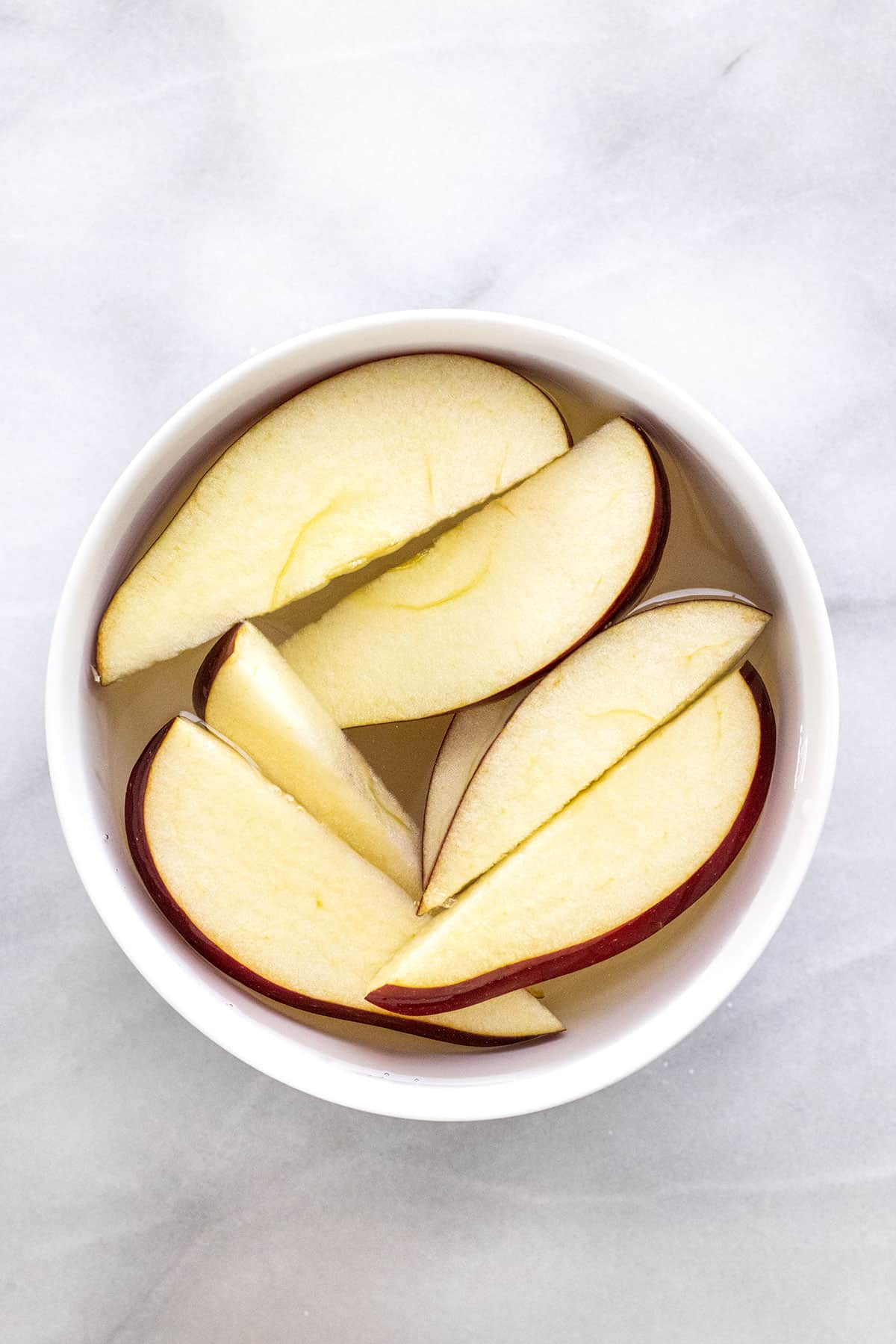 Slices of red apple inside a bowl of water.